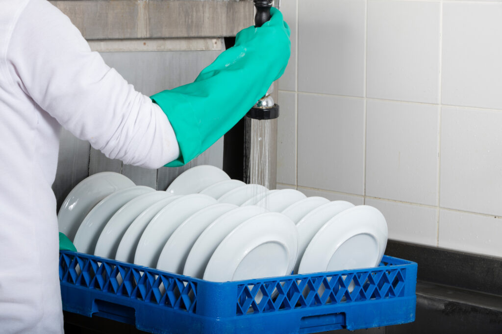 Dishes getting pre-rinsed before going through a large industrial kitchen dishwasher.